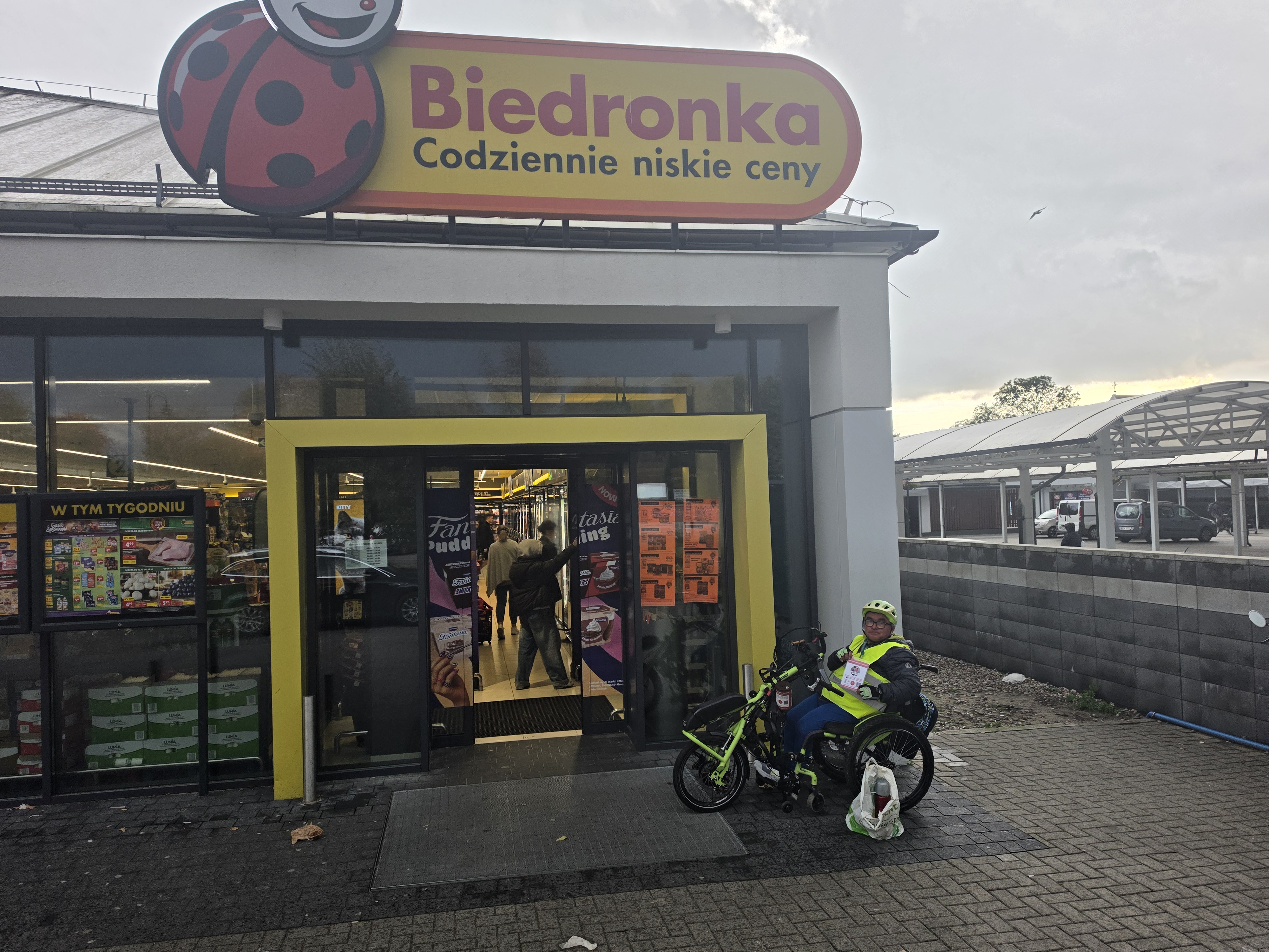 Zbyszek w żółtej kamizelce na handbike przy zbiórce pod Biedronką